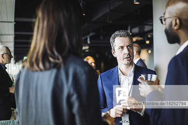 Businessman discussing with male and female colleagues while holding glass in office