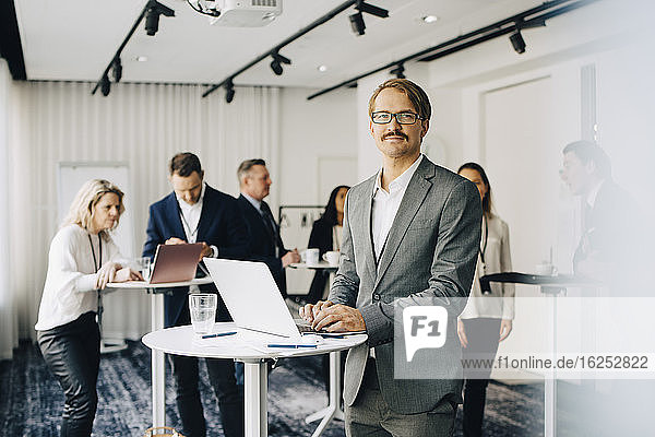 Portrait of businessman working over laptop while standing in office seminar