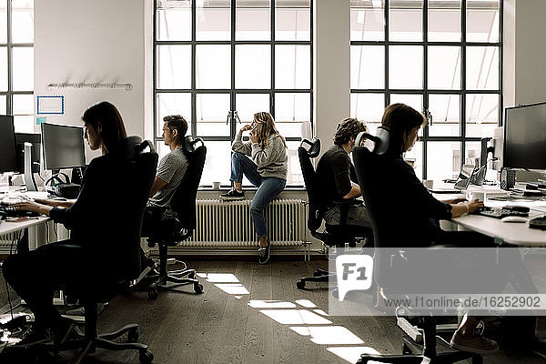 Coworkers working while female talking on phone in office