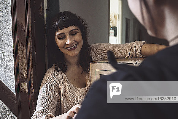 Smiling customer talking to delivery woman while holding package at doorstep