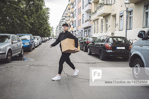 Zuversichtliche Zustellerin mit Pappkarton auf der Straße in der Stadt