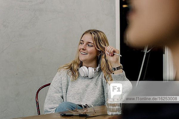 Lächelnde Geschäftsfrau mit Kopfhörern am Arbeitsplatz sitzend