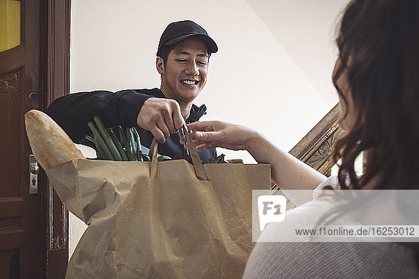 Lächelnder Lieferant liefert Gemüse an Kunden aus  während er vor der Tür spricht