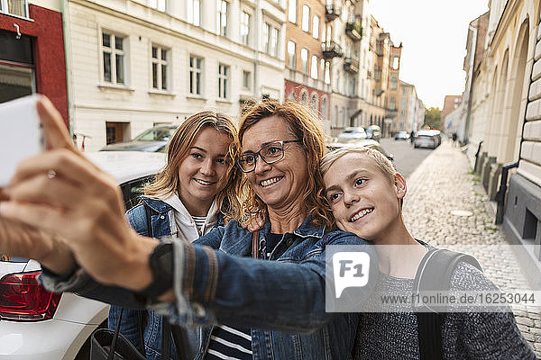 Lächelnde Mutter und Kinder  die sich am Wochenende am Straßenrand per Smartphone selbstständig machen