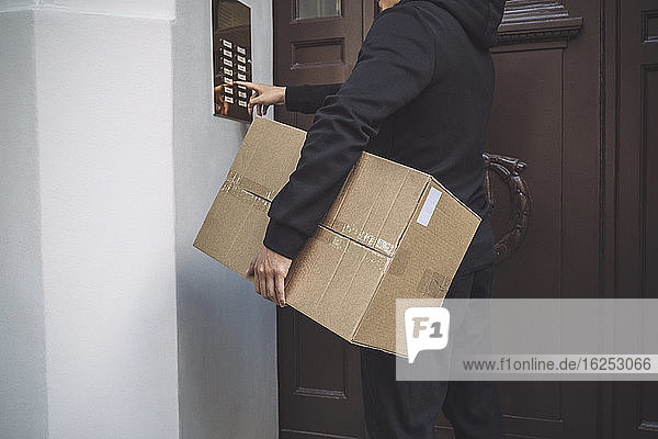 Midsection of delivery man ringing bell to deliver package at doorstep
