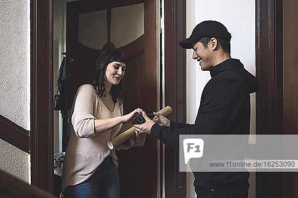 Smiling customer talking to delivery man while signing on smart phone at doorstep