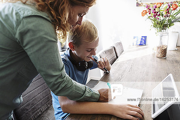 Mutter hilft lächelndem Sohn beim Lernen zu Hause