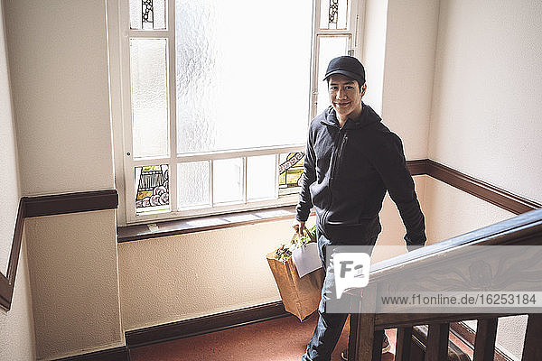 High angle portrait of smiling delivery man with package against window