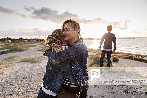 Lächelnde Mutter umarmt Tochter am Wochenende am Strand