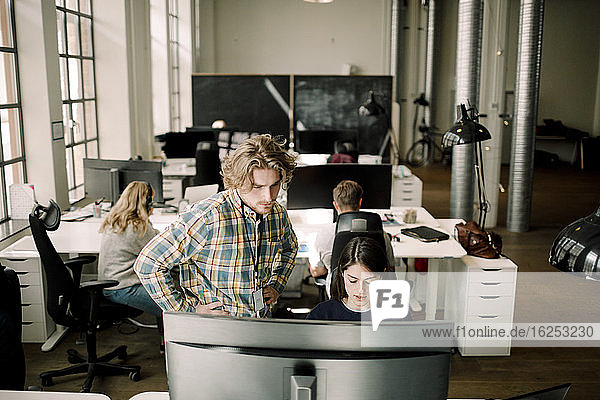 Geschäftsmann schaut auf Computer  während eine Kollegin im Büro sitzt