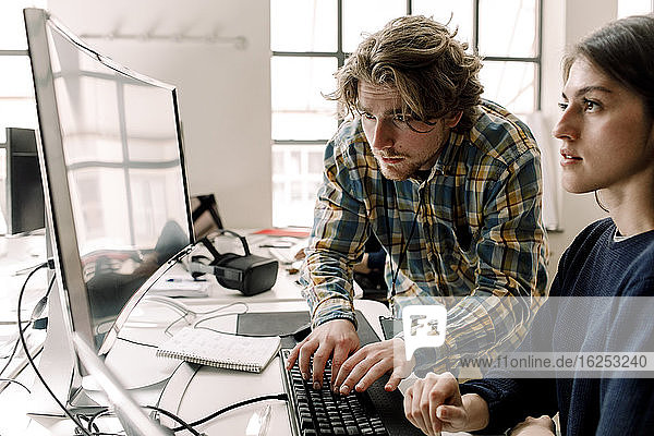 Businessman typing while coworker looking at computer in office