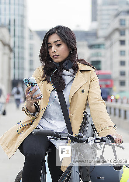 Woman on bicycle using smart phone in city