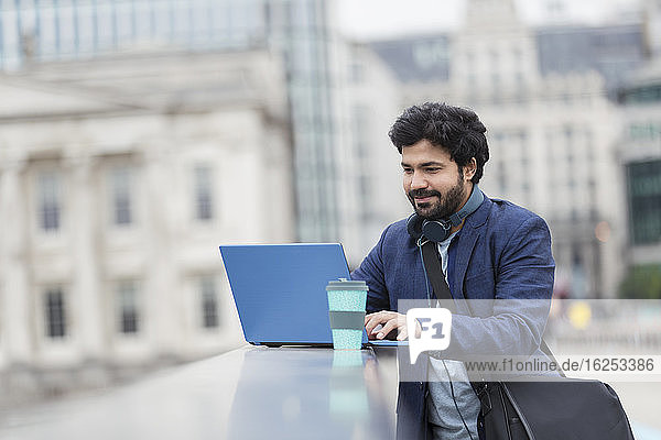 Geschäftsmann mit Laptop am Geländer der Stadtbrücke