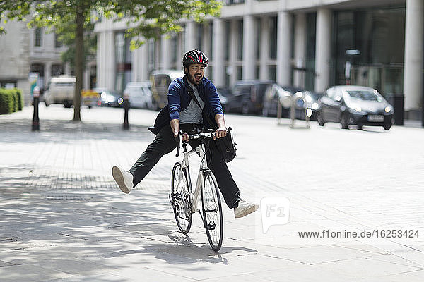 Verspielter Mann fährt Fahrrad auf sonniger Stadtstraße