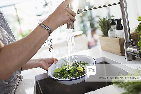 Frau wäscht Salat und Kräuter an der Küchenspüle