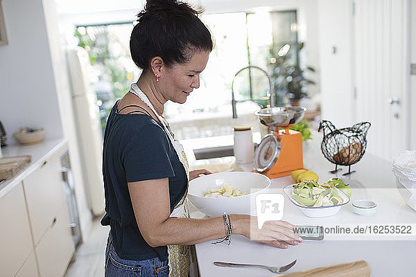 Frau mit Smartphone backt in der Küche