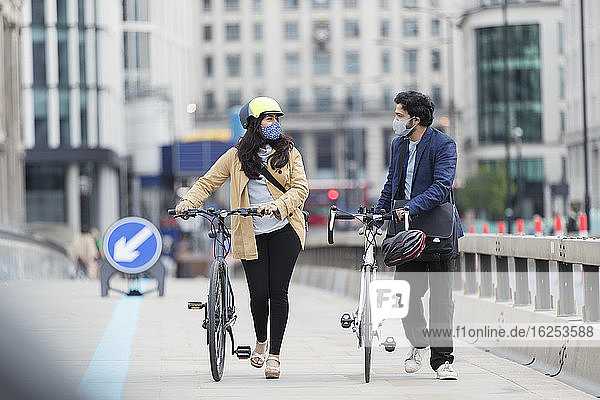 Geschäftsleute mit Gesichtsmasken beim Radfahren auf der städtischen Fußgängerbrücke