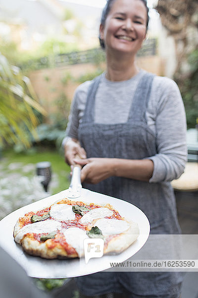 Porträt einer glücklichen Frau  die im Freien frische hausgemachte Pizza kocht