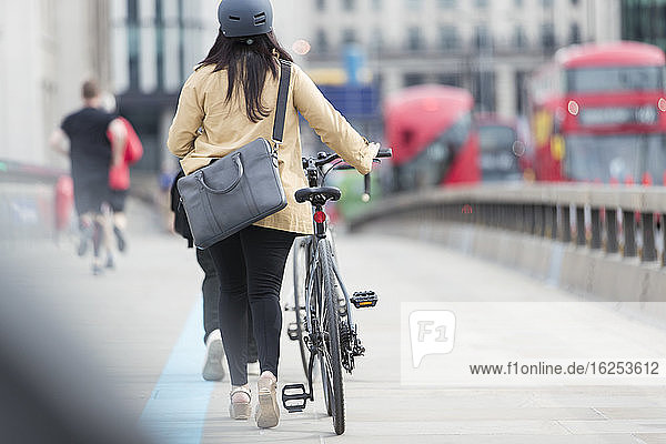 Geschäftsfrau zu Fuß mit dem Fahrrad entlang der Stadtbrücke  London  UK