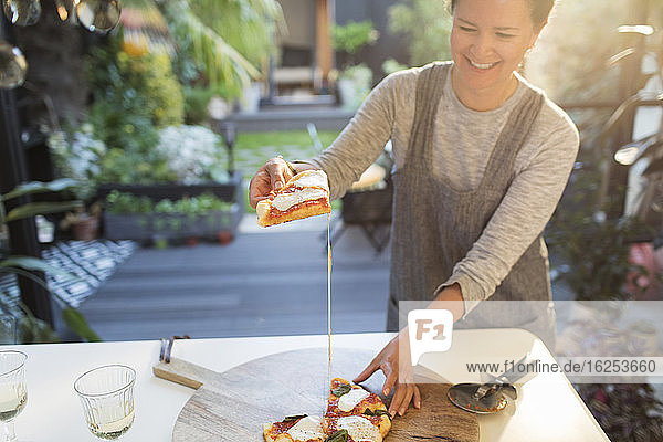 Lächelnde Frau isst hausgemachte Pizza auf der Terrasse