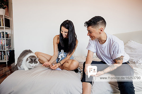Junges lesbisches Paar sitzt auf einem Bett und spielt mit einer Katze.