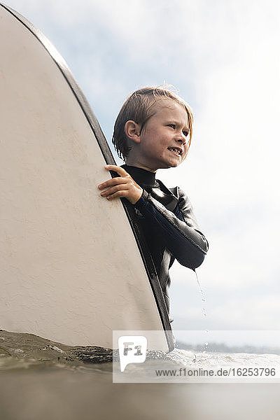 Portrait of young boy wearing wet suit, carrying surfboard into ocean, Santa Barbara, California, USA.