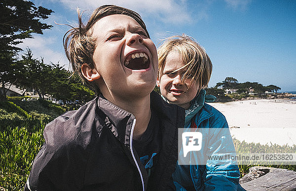 Two boys sitting by sandy beach near Carmel, California, USA, teasing each other.