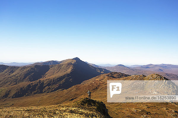 Einzelner männlicher Wanderer  der an einem sonnigen Tag auf einem Hügel steht und auf die Berge von Kerry in der Ferne schaut; Grafschaft Kerry  Irland
