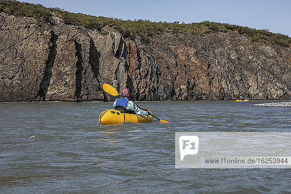 Two women paddling past rock feature on the Canning River in yellow packraft boats  Brooks Range  Arctic National Wildlife Refuge; Alaska  United States of America