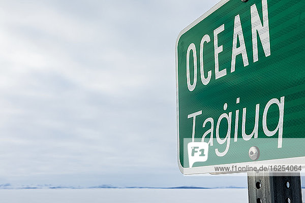 Straßenschild 'Ocean Tagiuq' im Winter  auf Englisch und Inupiaq  gegenüber dem Kotzebue-Sund im Winter; Kotzebue  Alaska  Vereinigte Staaten von Amerika