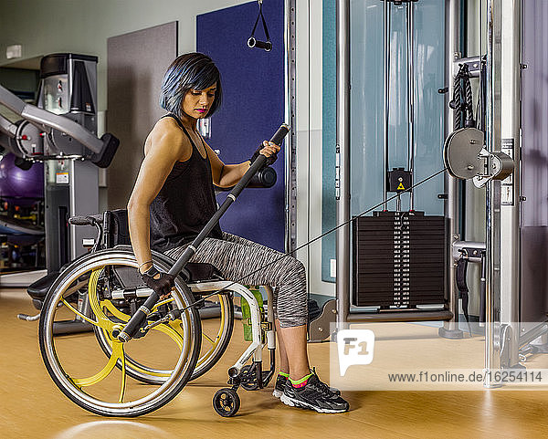 Ein Blick von der Seite einer querschnittsgelähmten Frau  die mit einer Stange trainiert  die mit einem Abzugsgerät in einer Fitnesseinrichtung verbunden ist; Sherwood Park  Alberta  Kanada