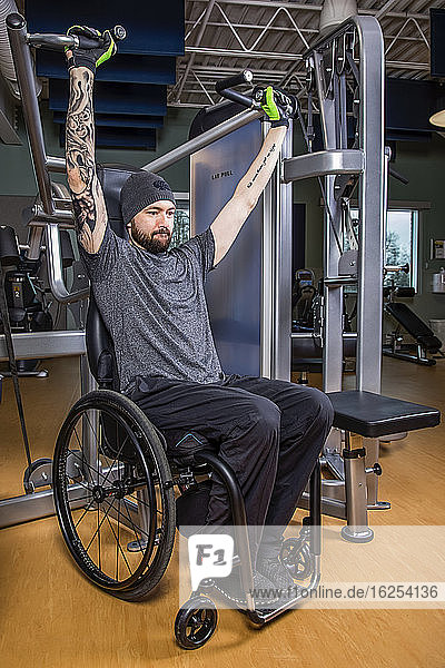 Ein querschnittsgelähmter Mann trainiert mit einer Überkopfpresse in einer Fitnessanlage; Sherwood Park Alberta Kanada
