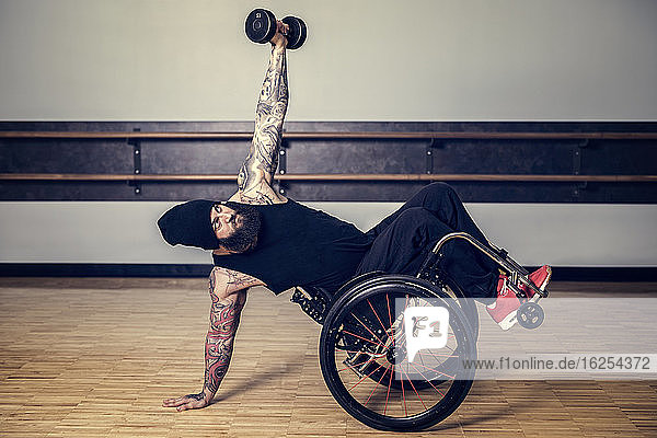Ein querschnittsgelähmter Mann  der nach dem Training in einer Fitnesseinrichtung in einer Turnhalle einen Rollstuhl in einen Rollstuhl setzt und balanciert  während er ein Gewicht hebt: Sherwood Park  Alberta  Kanada