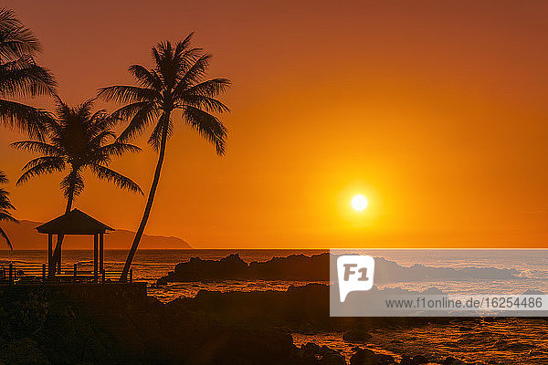 Sonnenuntergang am orangefarbenen Himmel mit silhouettiertem Felsen Pavillon und Palmen entlang der Uferpromenade; Oahu Hawaii Vereinigte Staaten von Amerika