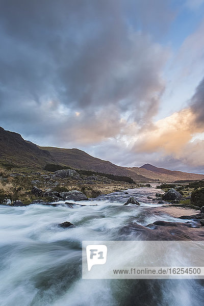 Wildwasserfluss stürzt bei Sonnenuntergang mit dramatischem Himmel durch das Schwarze Tal im Herzen der Kerry-Berge; Grafschaft Kerry  Irland