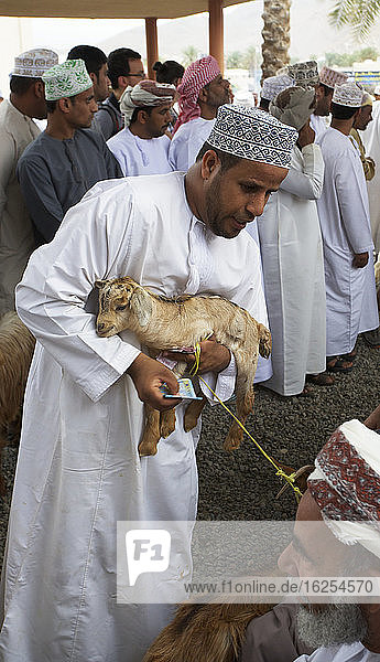 Traditionally Dressed Omani Men Inspecting Goats In The Goat Market At The Friday Souk