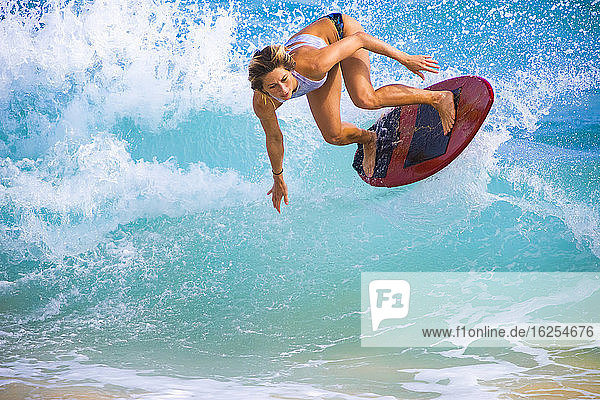 Eine junge Frau springt auf einem Skimboard vor Sandy Beach (Oahu) in die Luft; Oahu Hawaii Vereinigte Staaten von Amerika