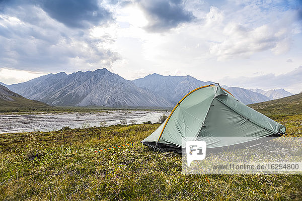 Grün-graues Rucksackzelt  das im Sommer in der Tundra aufgestellt wird  an einem Sommertag in den Brooks Range-Bergen  Arctic National Wildlife Refuge  mit dem Marsh Fork River im Hintergrund; Alaska  Vereinigte Staaten von Amerika