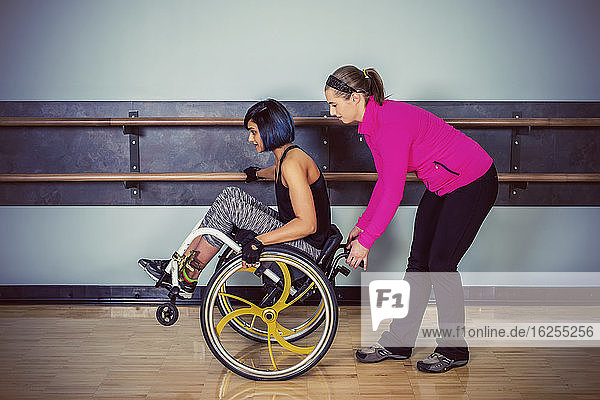 A paraplegic woman popping wheelie in her wheelchair and fooling around in a gymnasium with her personal trainer after working out at a fitness facility: Sherwood Park  Alberta  Canada