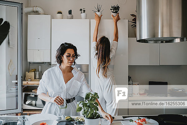 Zwei lächelnde Frauen mit braunem Haar stehen in einer Küche und bereiten Essen zu.
