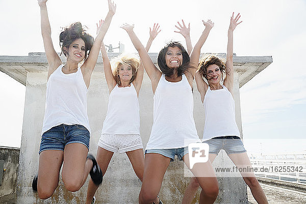 Porträt von vier jungen Frauen  die Spaß haben  mit erhobenen Armen in die Luft springen und in die Kamera schauen.