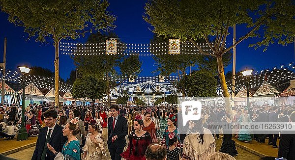 Feiernde Spanier in traditioneller Kleidung vor beleuchteten Festzelten  Casetas am Abend  geschmückte Straße  Feria de Abril  Sevilla  Andalusien  Spanien  Europa