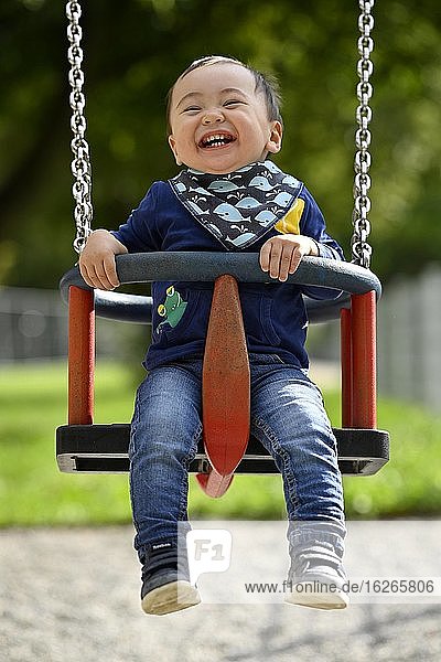 Toddler  boy  14 months  multi-ethnic  on children's swing  laughs  Blaubeuren  Baden-Württemberg  Germany  Europe