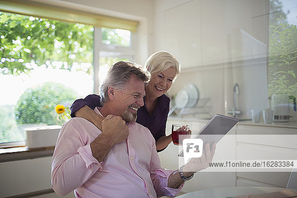 Glückliches älteres Ehepaar benutzt digitales Tablett in der Küche