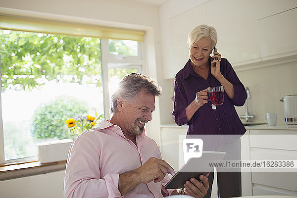 Glückliches älteres Ehepaar mit digitalem Tablet und Smartphone in der Küche