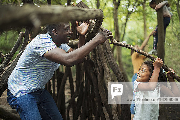 Father and daughter building teepee with branches in woods