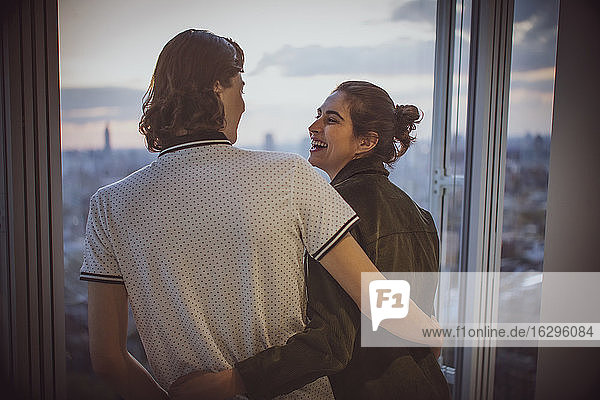 Glückliches junges Paar umarmt sich am Hochhausfenster