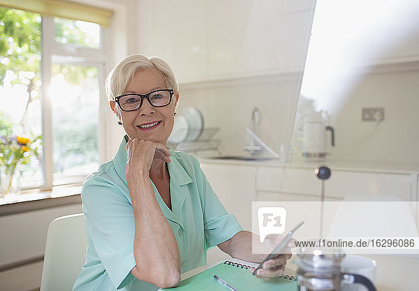 Porträt einer selbstbewussten älteren Frau  die ein Smartphone in der Morgenküche benutzt