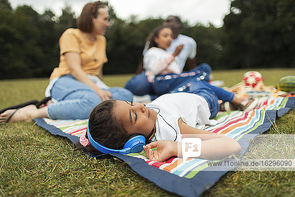 Girl with headphones relaxing and listening to music on picnic blanket