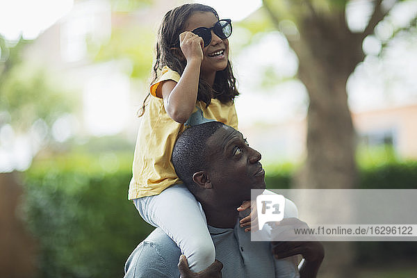 Vater trägt Tochter mit Sonnenbrille auf den Schultern